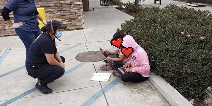Two girls sit in a parking lot, finishing their homework on computers, while two Taco Bell employees talk to them.