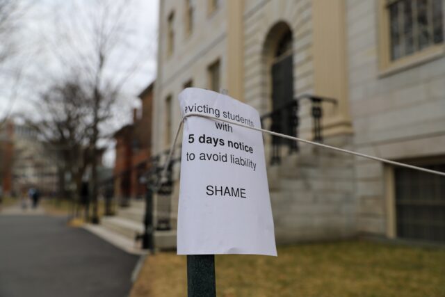 A sign hangs outside a Harvard building, reading “Evicting students with 5 days notice to avoid liability. Shame”